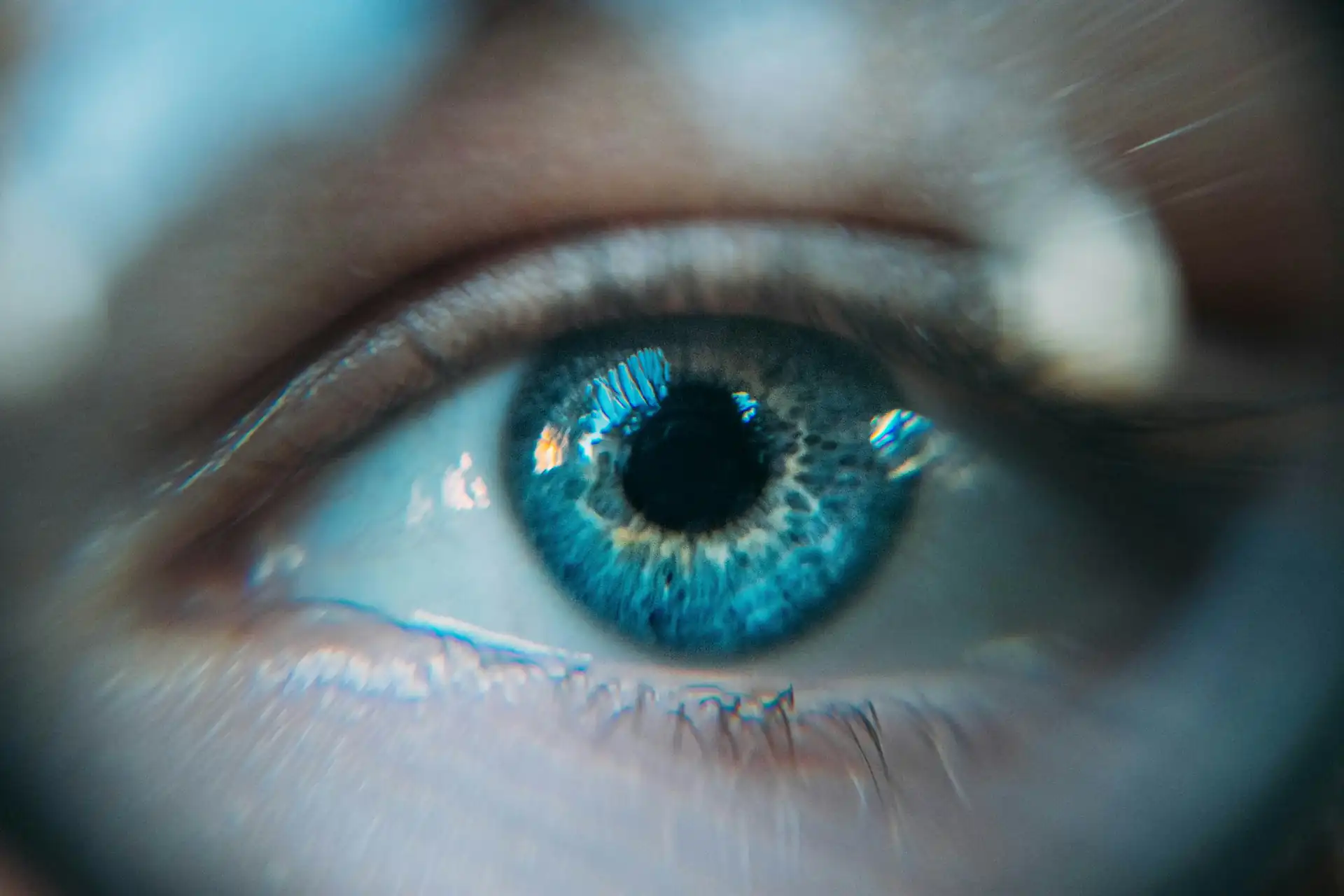 Close-up of an eye with a blue iris and light reflected on the cornea
