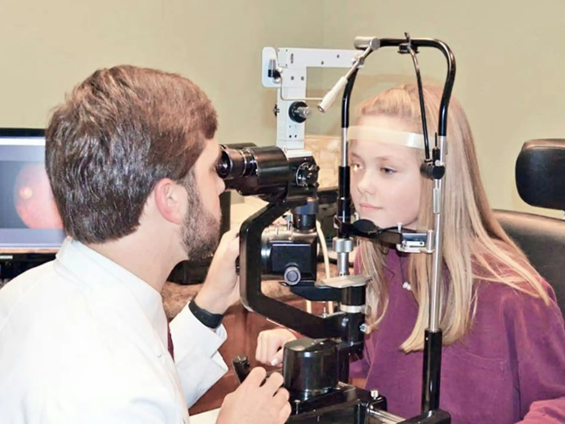 Ophthalmologist examining a patient's retina with a slit lamp, with a retinal image on the screen