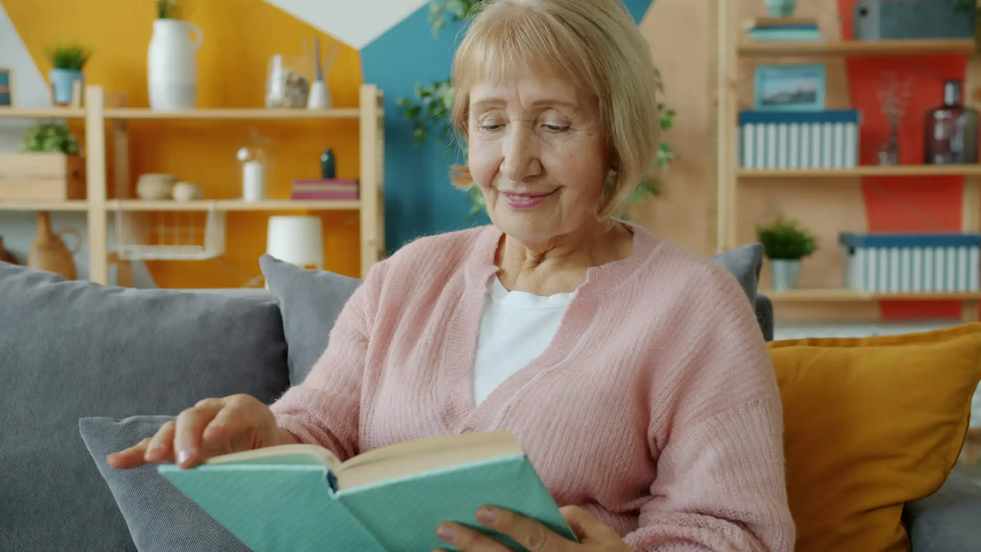 Older woman reading a book without glasses on the sofa at home